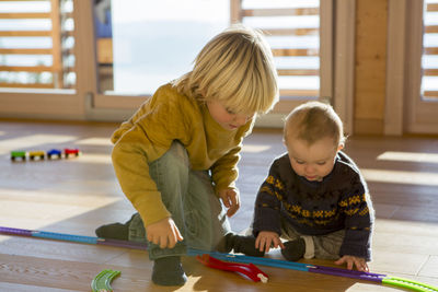 Little boy and his brother playing with toy train on the wooden floor at home