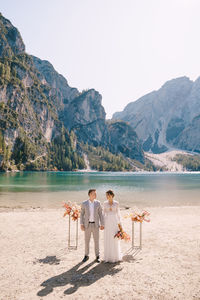 Bridegroom standing on lakeshore against clear sky