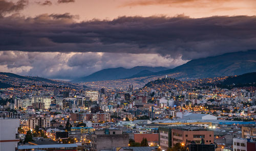 Illuminated cityscape against cloudy sky at dusk