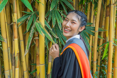 Portrait of happy young woman standing by bamboos