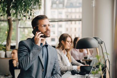 Businessman talking on mobile phone while sitting with colleague at creative office