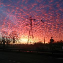 Silhouette trees and electricity pylon against sky during sunset