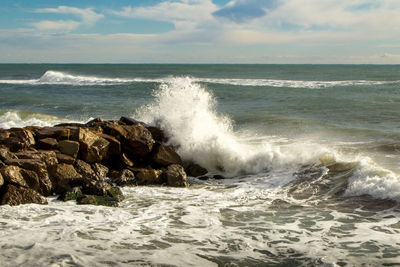 Scenic view of sea and waves splashing against the rocks in windy day