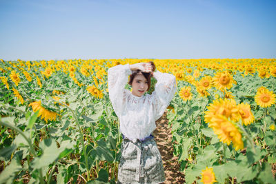 Woman standing on sunflower field against sky