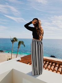 Woman standing on retaining wall at terrace against sea