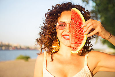 Portrait of woman holding watermelon on face against clear sky