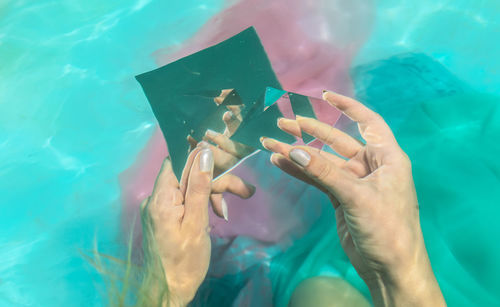 Cropped hand of woman holding pyramid crystal in swimming pool