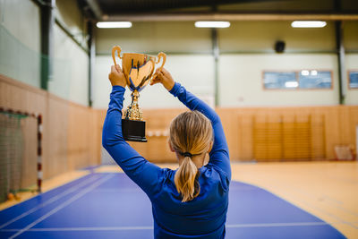 Rear view of girl holding golden trophy while standing in sports court