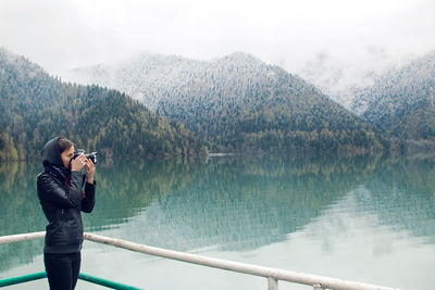 Woman in a leather jacket with a camera taking pictures ritsa lake in the spring morning