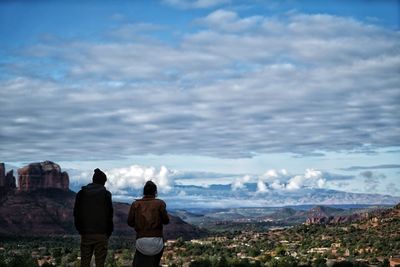 Rear view of men on landscape against cloudy sky