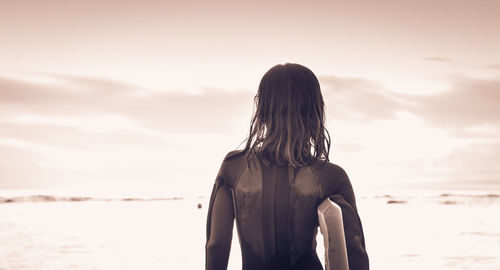 Rear view of girl standing at beach against sky