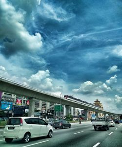 Cars on road in city against dramatic sky