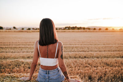 Rear view of woman sitting on grassy land at sunset