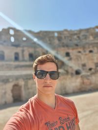 Portrait of young man wearing sunglasses standing against old ruins
