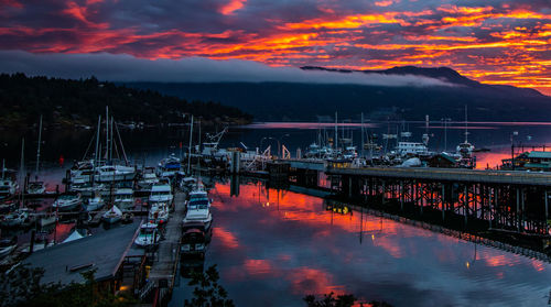 Sailboats moored at harbor against sky during sunset