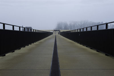 Empty footbridge in fog against sky