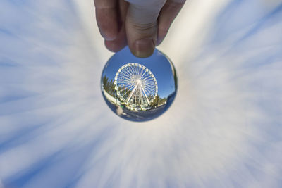 Cropped hand holding crystal ball with reflection of ferris wheel