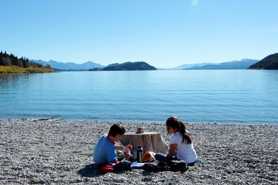 People relaxing on lake against clear sky