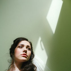 Thoughtful young woman looking up against green wall