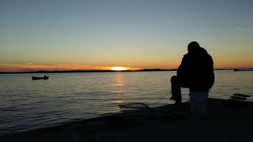 Silhouette man standing on beach against clear sky during sunset