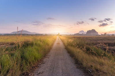 Road amidst field against sky during sunset