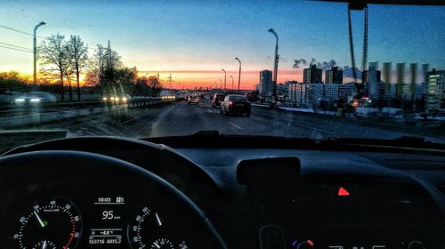 Cars on road in city against sky during sunset