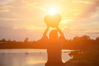 Silhouette woman standing by lake against sky during sunset