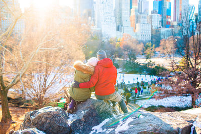 Rear view of men sitting on rock by trees in city