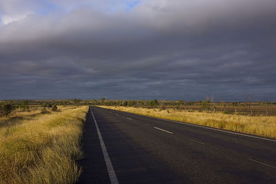 Driving into a storm at sunset along road bordered by golden dry grass.