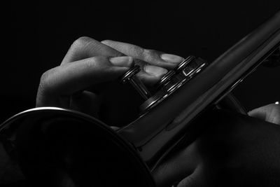 Cropped hand playing trumpet against black background