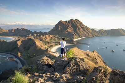 Man standing on rock by sea against sky