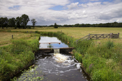 Stream flowing amidst field against sky
