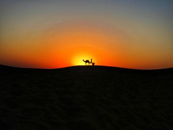 Silhouette man riding camel against sky during sunset