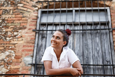 Portrait of smiling young woman against brick wall