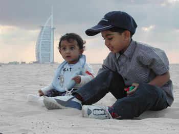 Siblings sitting on beach with burj al arab in background