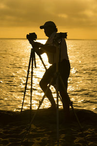 Silhouette man photographing sea against sky during sunset