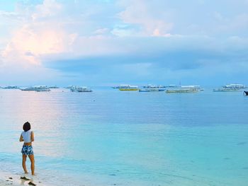 Rear view of woman standing on shore at beach against cloudy sky