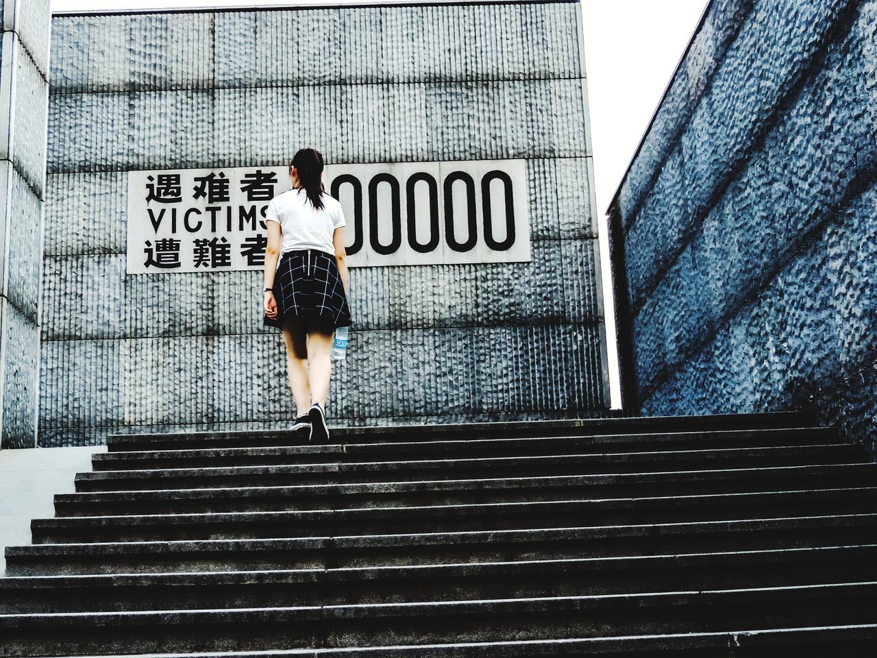 REAR VIEW OF WOMAN ON STAIRCASE AGAINST WALL