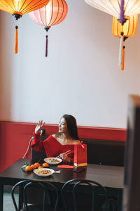 Beautiful young asian woman in red clothes eating asian food in festive chinese vietnamese cafe