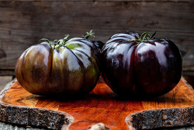 Whole raw ripe american black heirloom tomatoes on reddish wood cutting board
