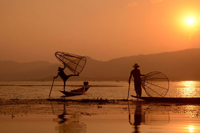 Silhouette men fishing in lake at sunset