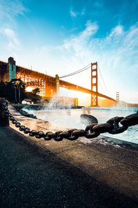 View of suspension bridge over river against cloudy sky