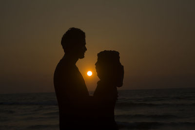 Silhouette couple standing face to face at beach against clear sky