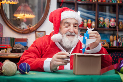 Senior man in santa claus costume sitting at home