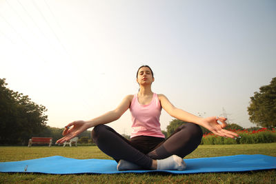 Portrait of young woman sitting on field against clear sky