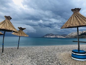 Thatched roof parasols at beach against cloudy sky