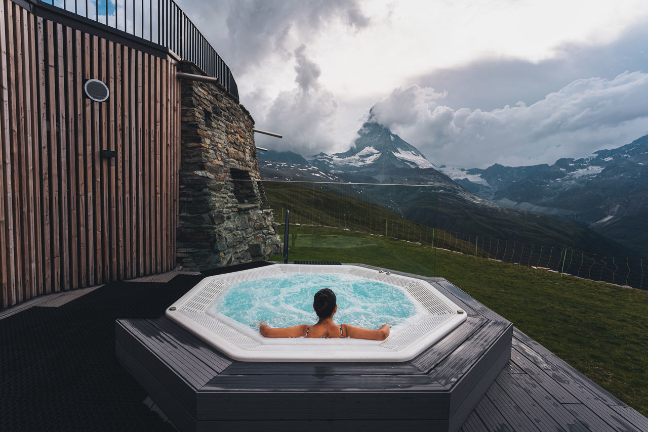 cloud - sky, one person, mountain, sky, rear view, water, lifestyles, nature, leisure activity, real people, swimming pool, day, pool, beauty in nature, architecture, scenics - nature, mountain range, relaxation, outdoors, hot tub