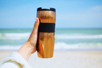 Midsection of woman holding drink at beach against sky