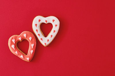 Two decorated with icing and glazed heart shape cookies on red background with copy space.