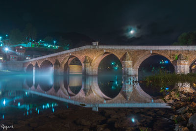 Illuminated bridge over river in city against sky at night